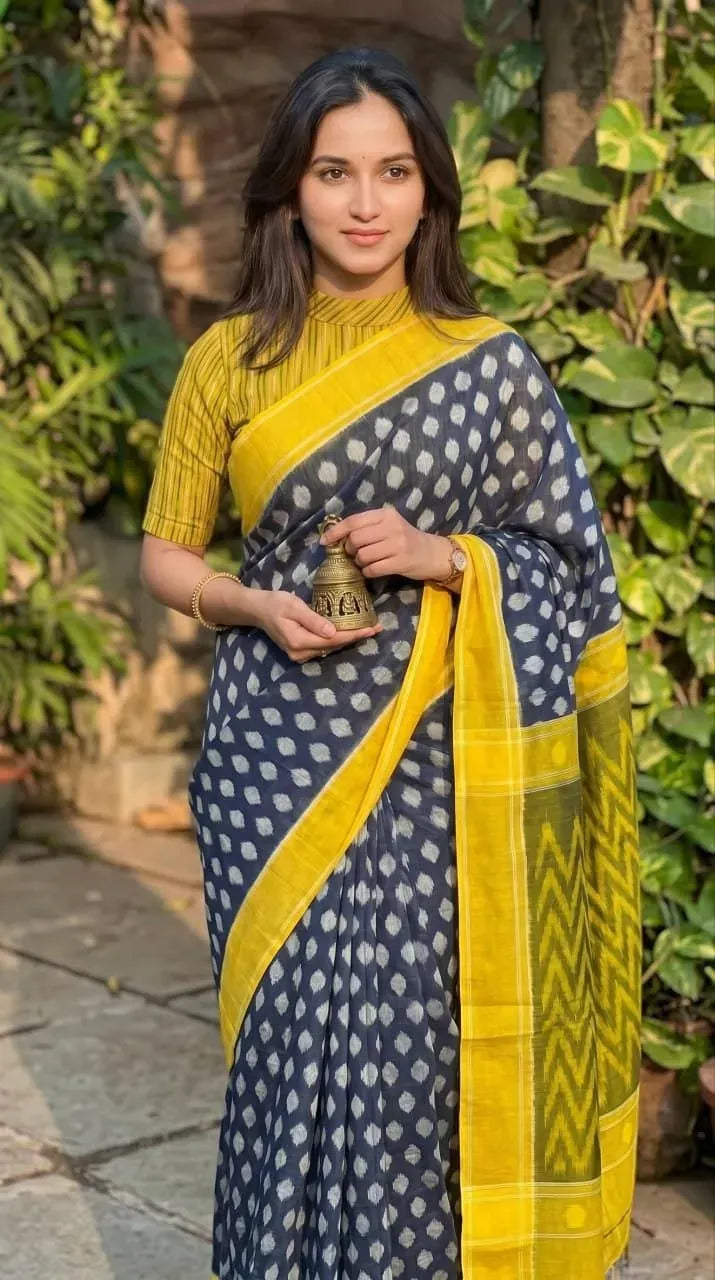 Model wearing blue and yellow digital print linen saree holding a small brass bell