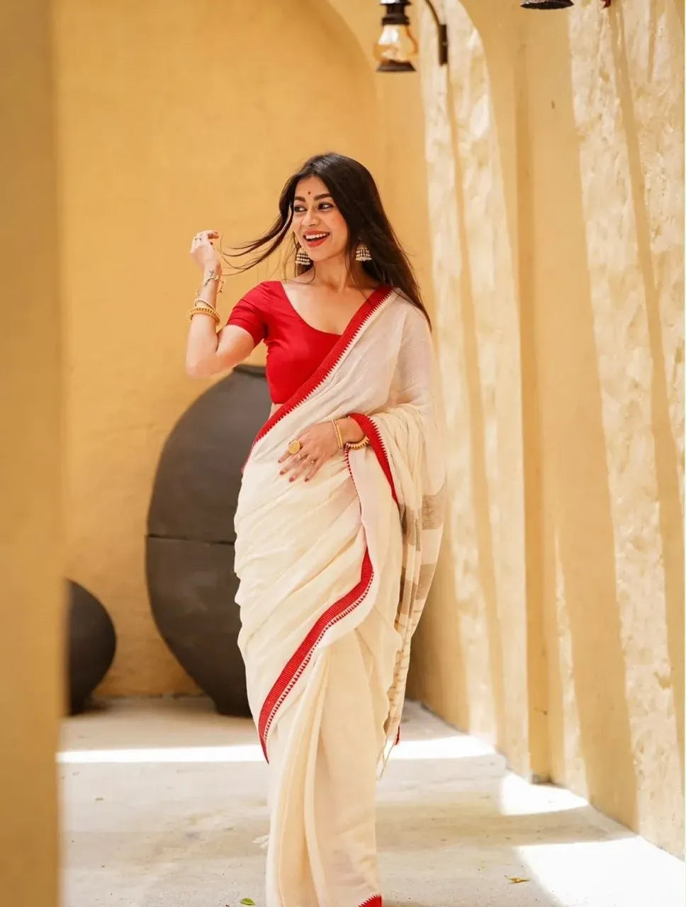 Model wearing off-white linen saree with red border near arched wall