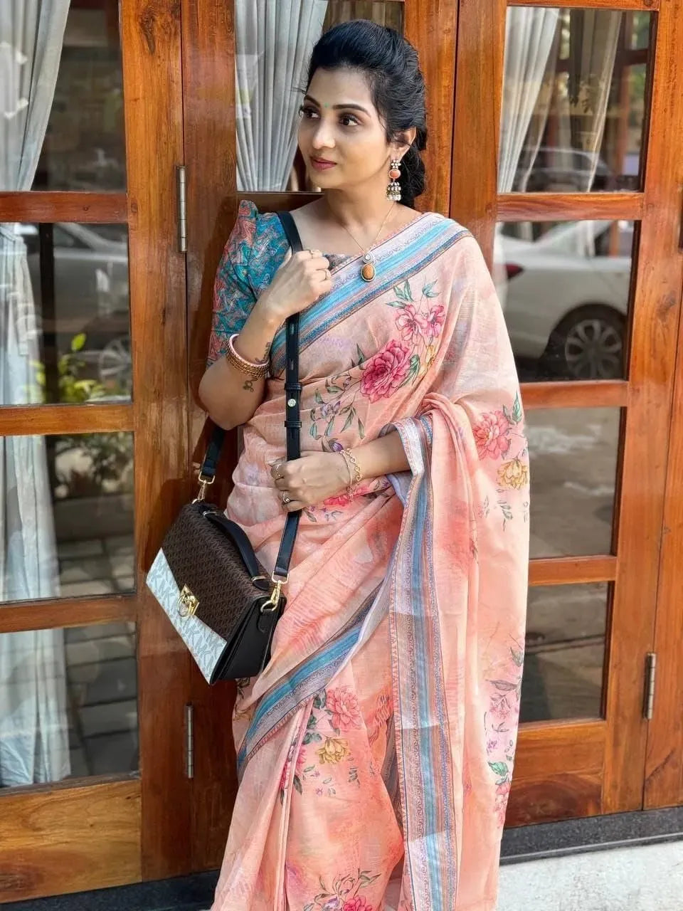 Model posing near wooden doors wearing peach floral print linen saree with blue blouse