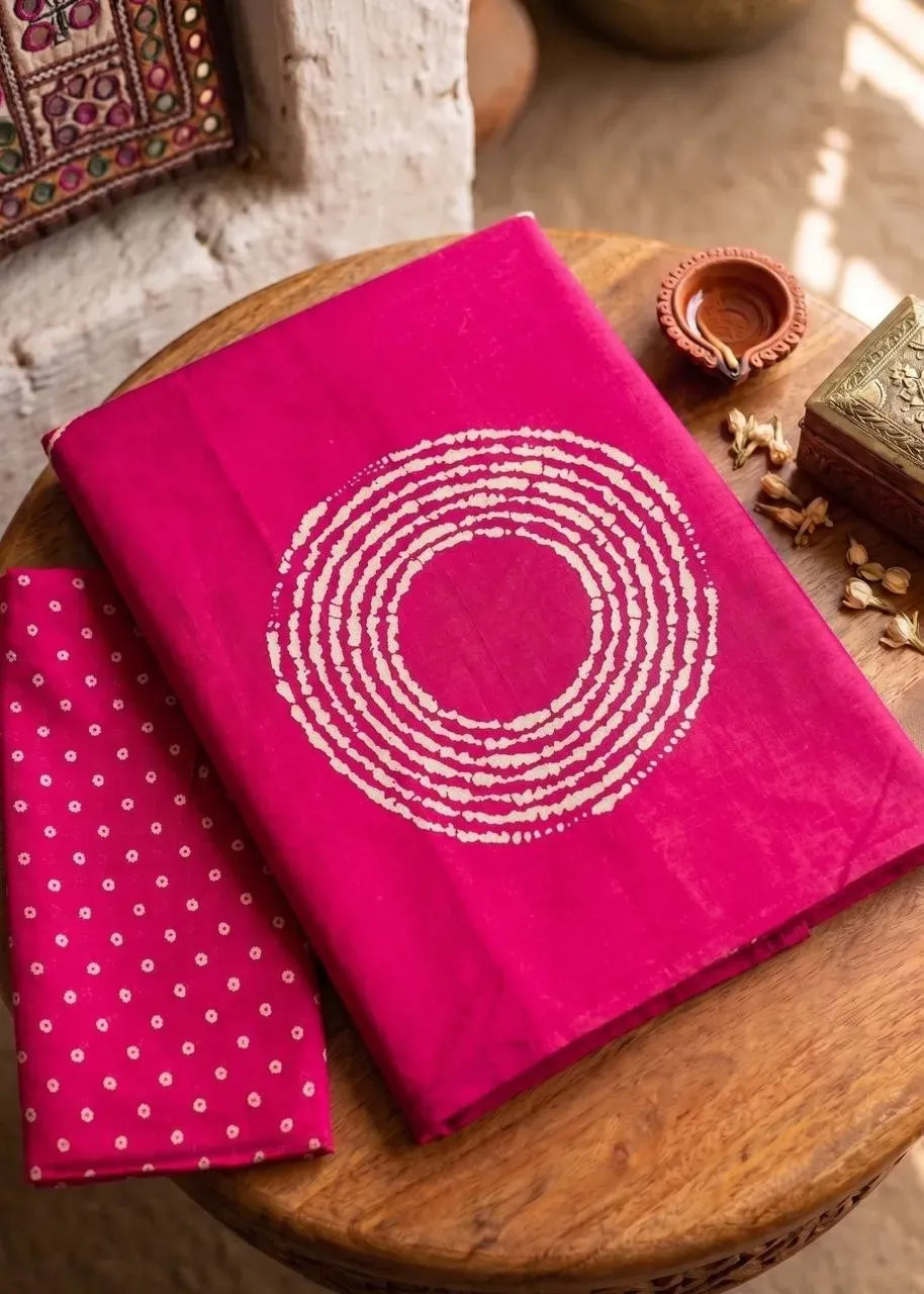 Magenta pink pure mul cotton saree folded on wooden table with diya