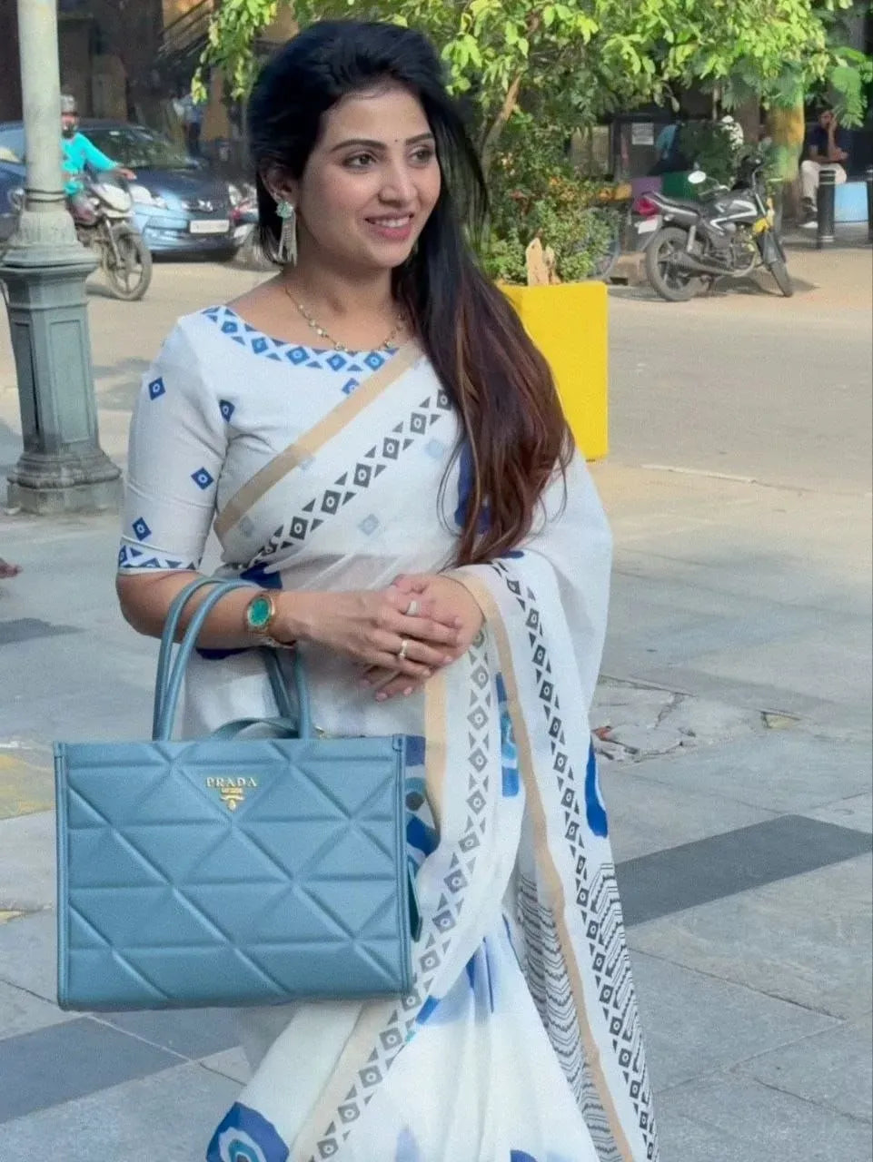 Model wearing white soft linen saree with blue evil eye print holding handbag