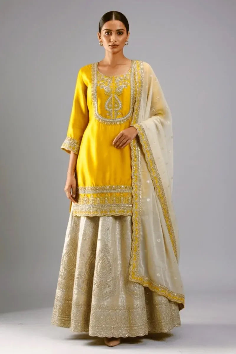 Model wearing yellow chinnon silk top with embroidered sharara and dupatta