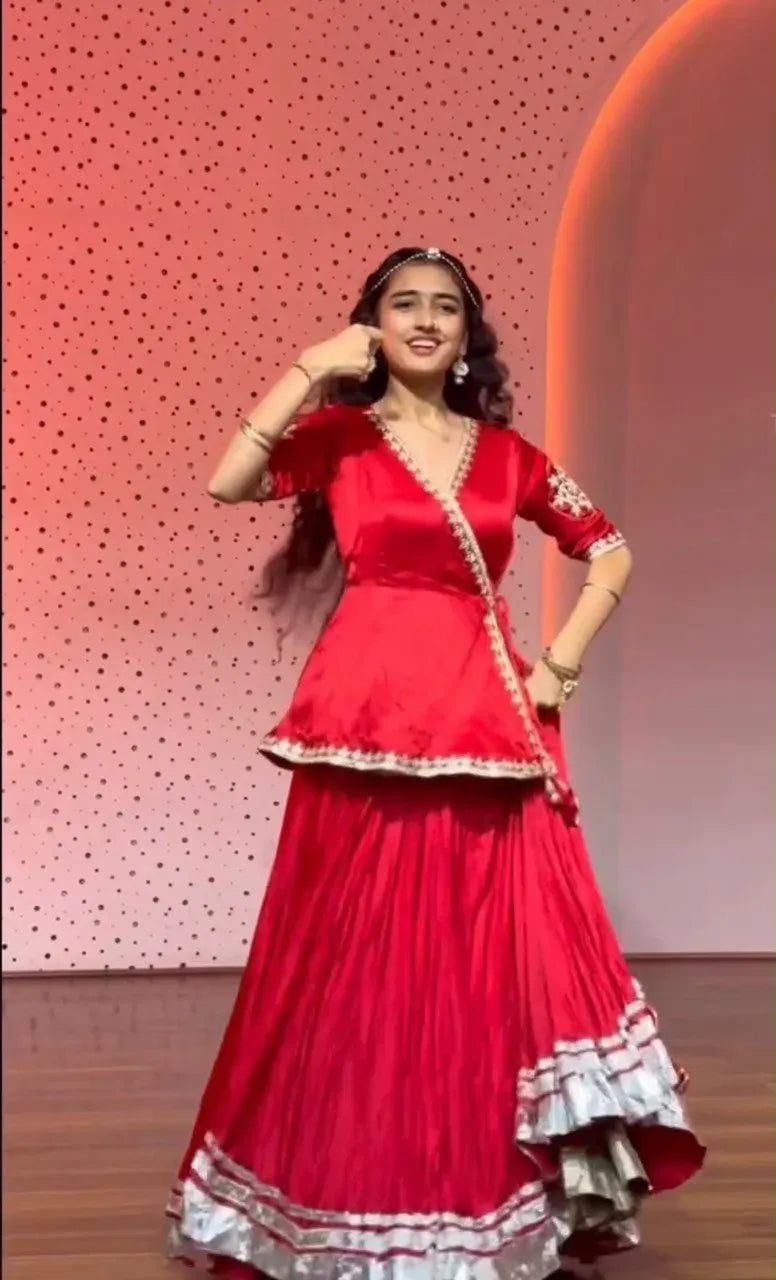 Model wearing red crepe silk lehenga choli posing gracefully against pink patterned backdrop