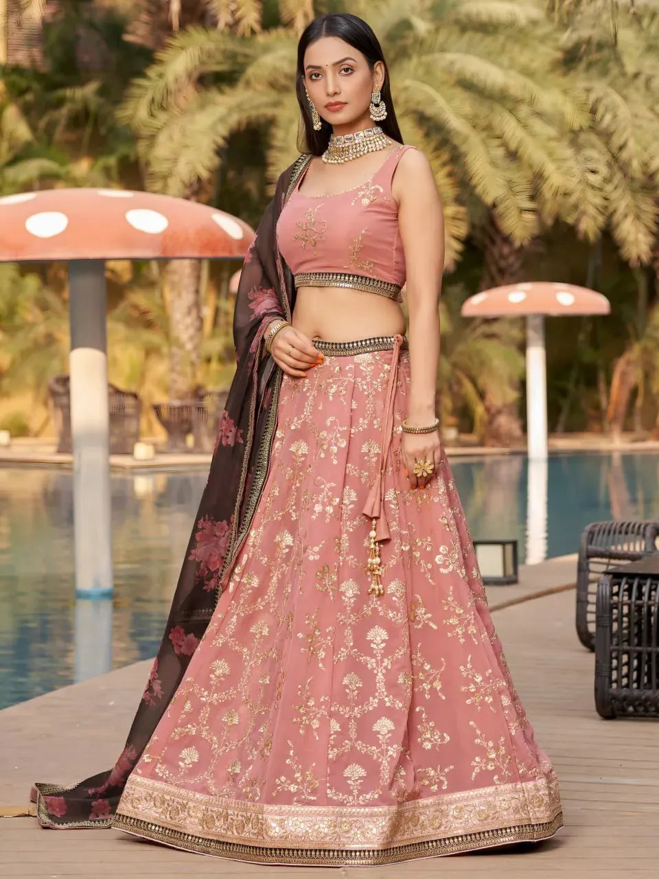 Model wearing dusty pink georgette lehenga with gold embroidery and black dupatta by pool
