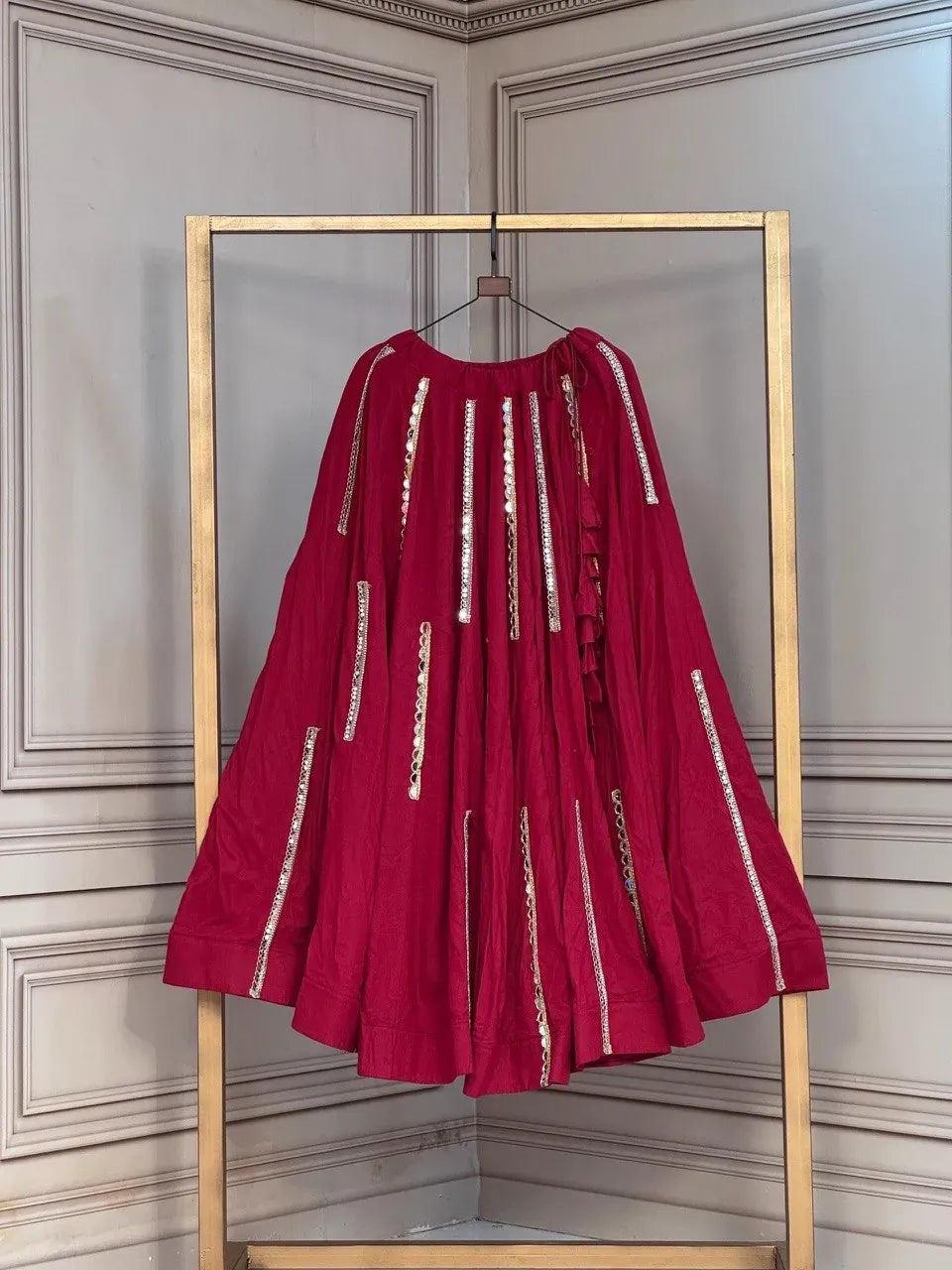 Maroon rayon lehenga with intricate mirror work lace hanging on a gold stand