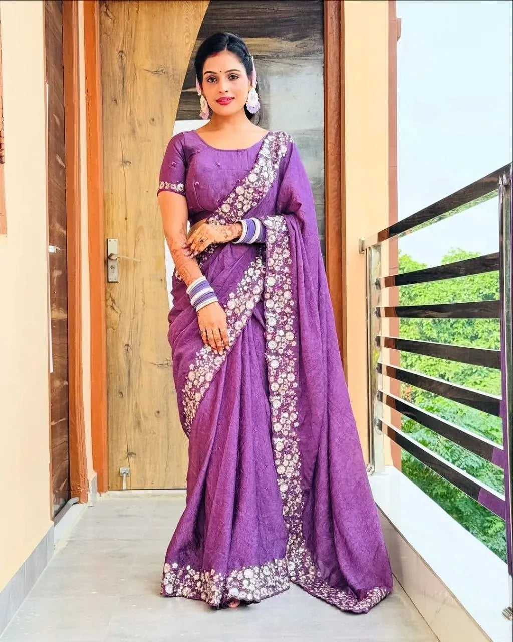 Woman wearing purple designer saree with heavy embroidery standing on balcony