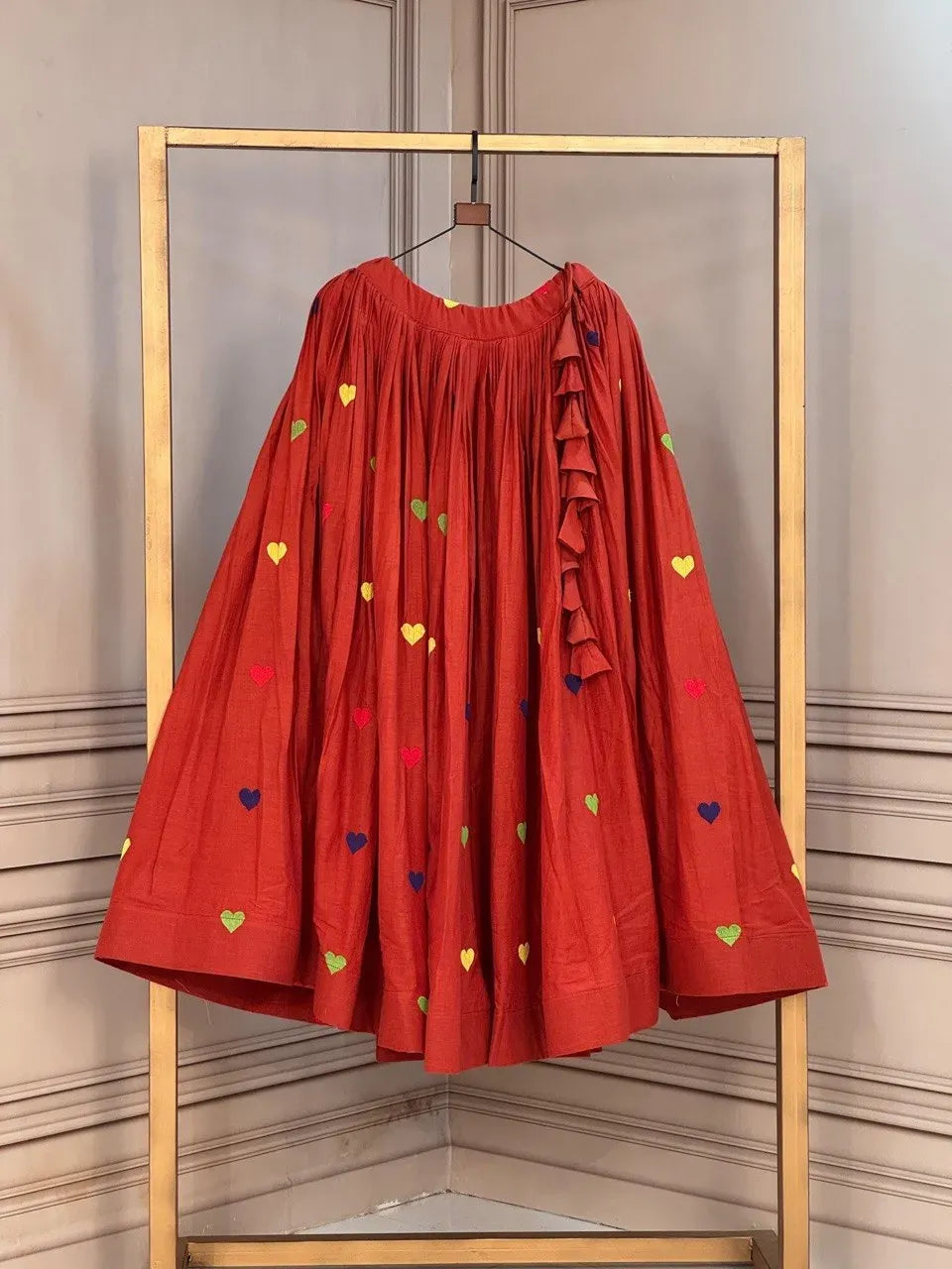 Red cotton lehenga hanging on a golden rack with colorful embroidered hearts