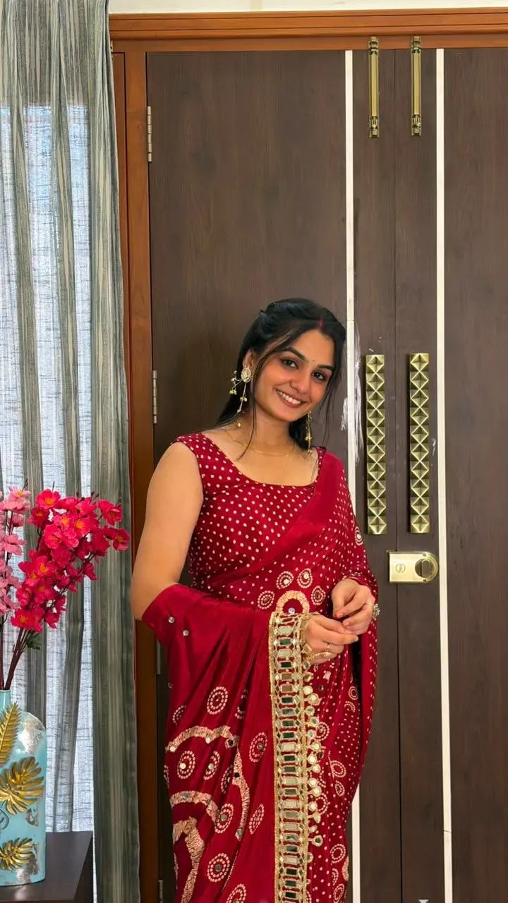 Smiling woman wearing a deep red bandhani saree posing indoors