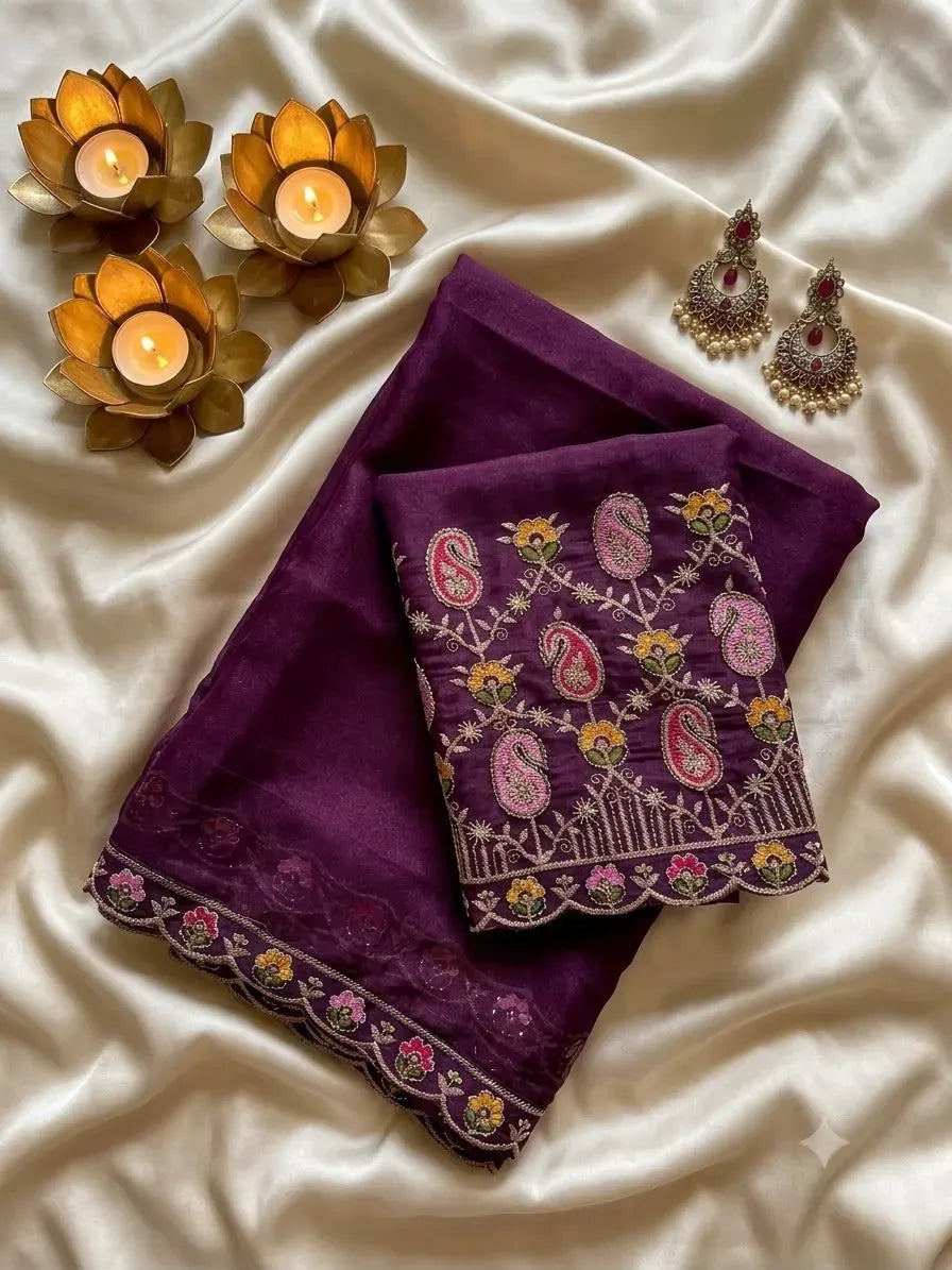 Deep purple georgette saree folded neatly with embroidered blouse piece and matching earrings on silk cloth