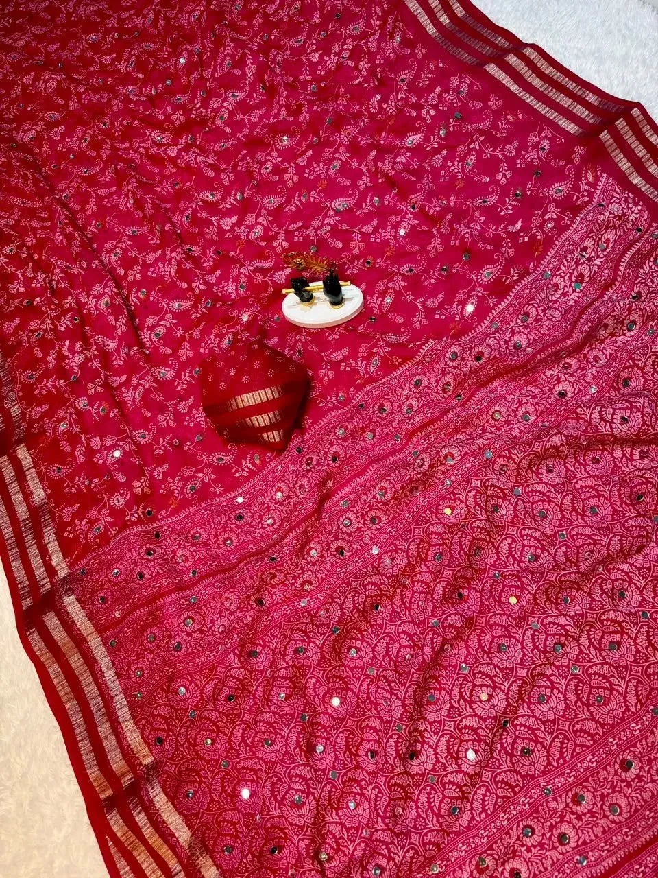 Pink georgette saree flat lay with intricate mirror work and matching blouse piece