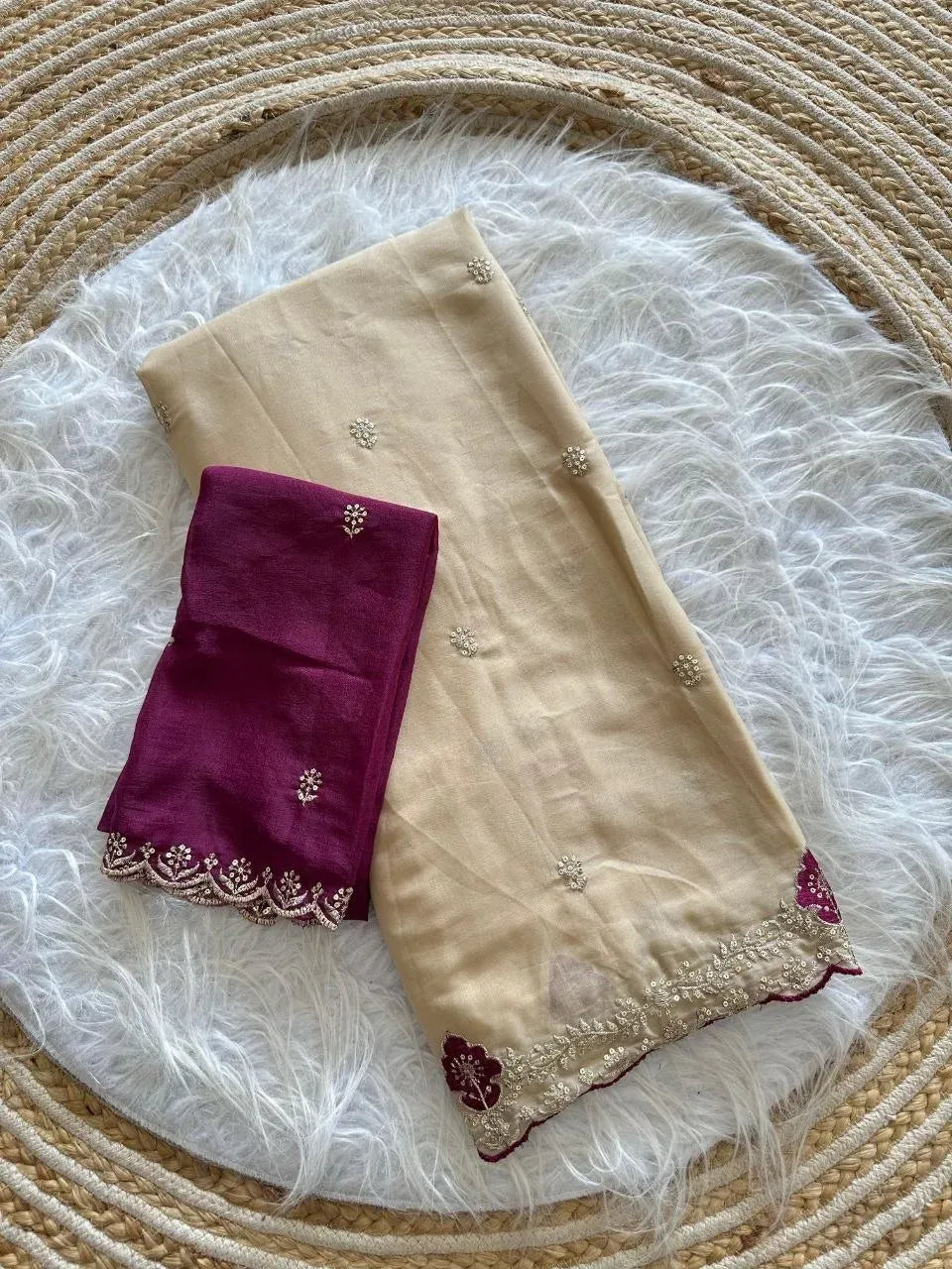Beige georgette saree folded neatly with a contrasting maroon embroidered blouse piece