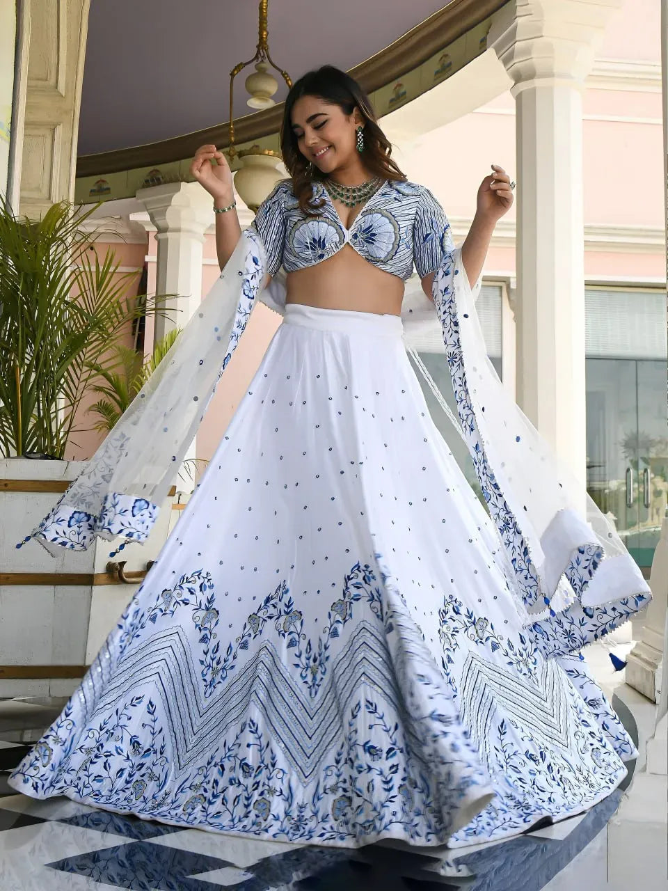 Model wearing white lehenga choli with blue floral embroidery and sheer dupatta