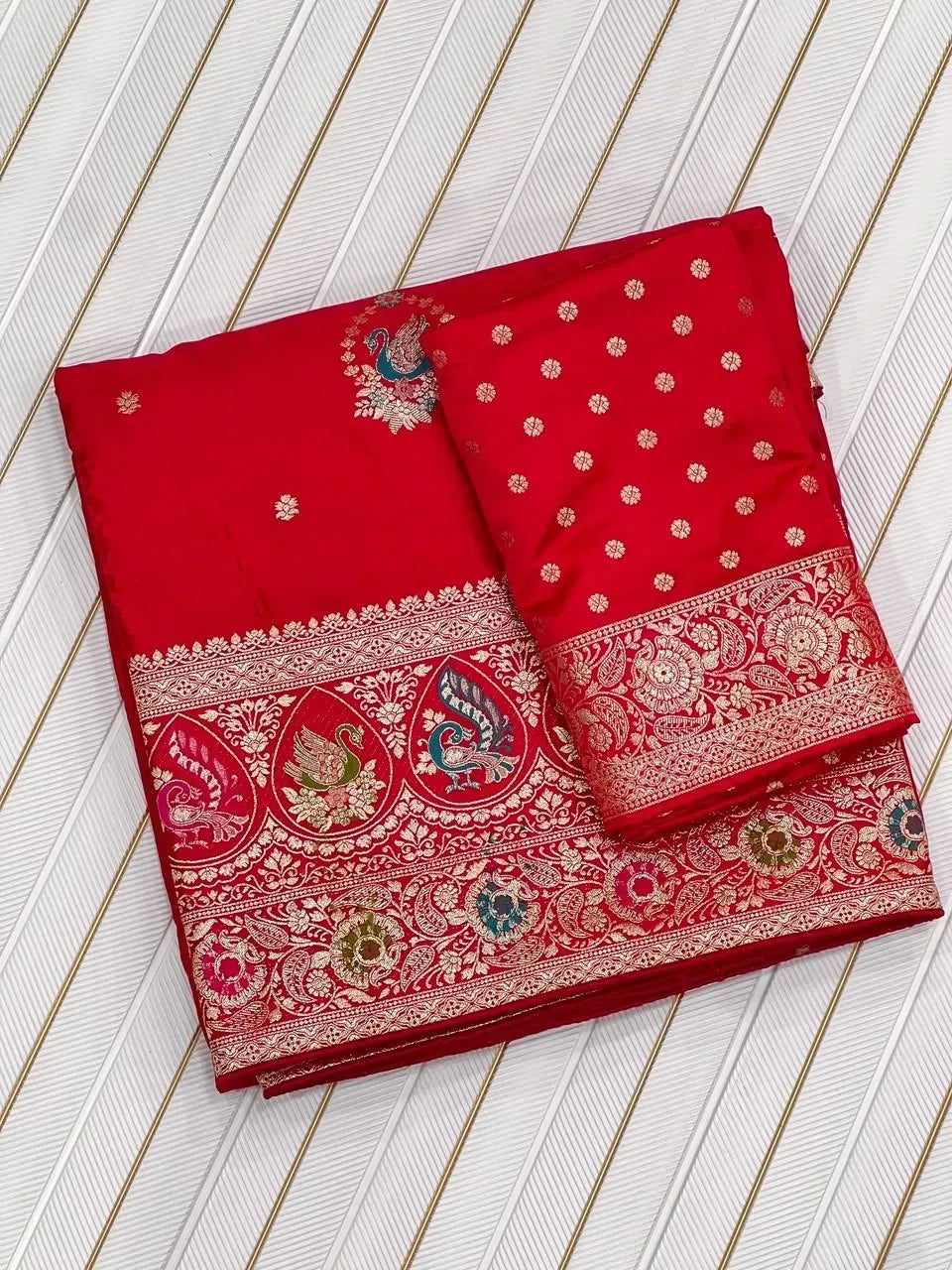 Folded red satin silk saree with ornate zari weaving border and unstitched blouse