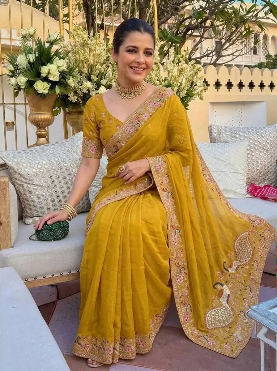 Model sitting gracefully in yellow georgette party wear saree holding a green clutch