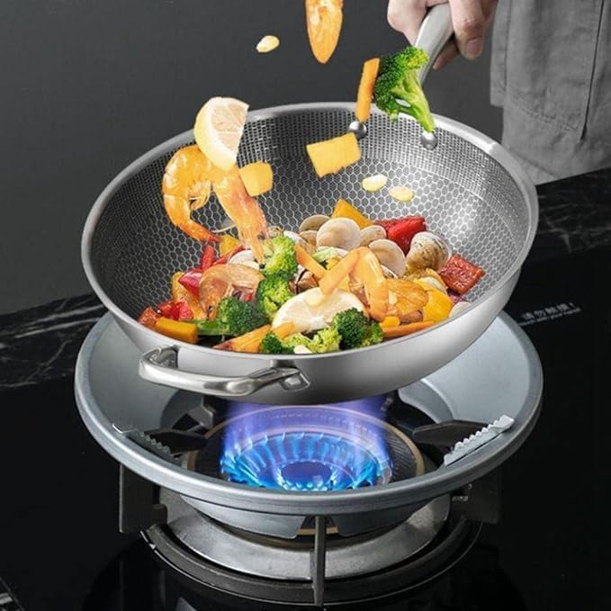 Stainless steel wok with food being added over a lit stove