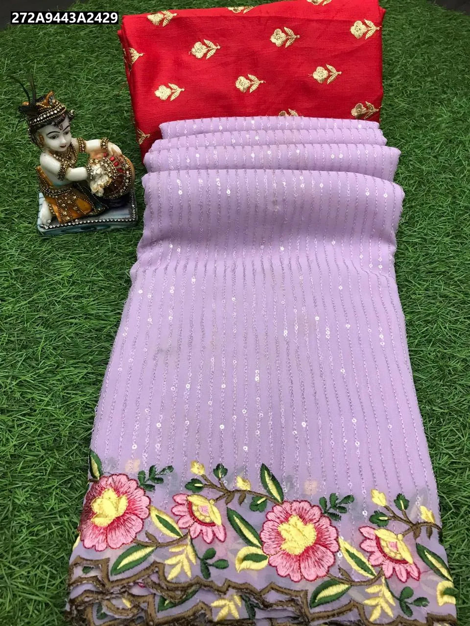 Flat lay of a Lavender Georgette Sequence Saree with intricate floral cutwork border, paired with a red Butti work blouse, on green grass.