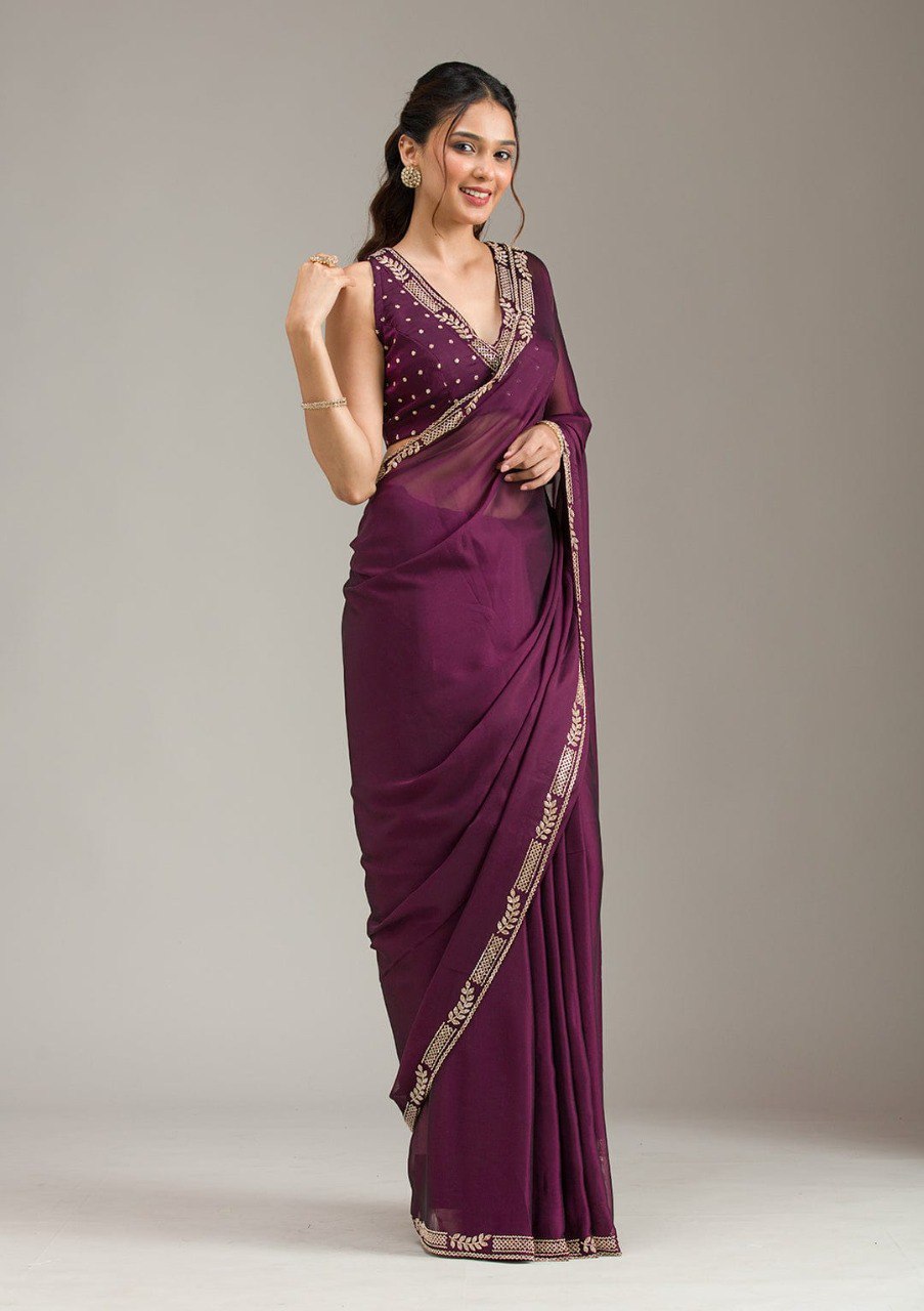 Woman elegantly draped in a purple georgette saree with gold zarkan work, paired with a matching blouse.