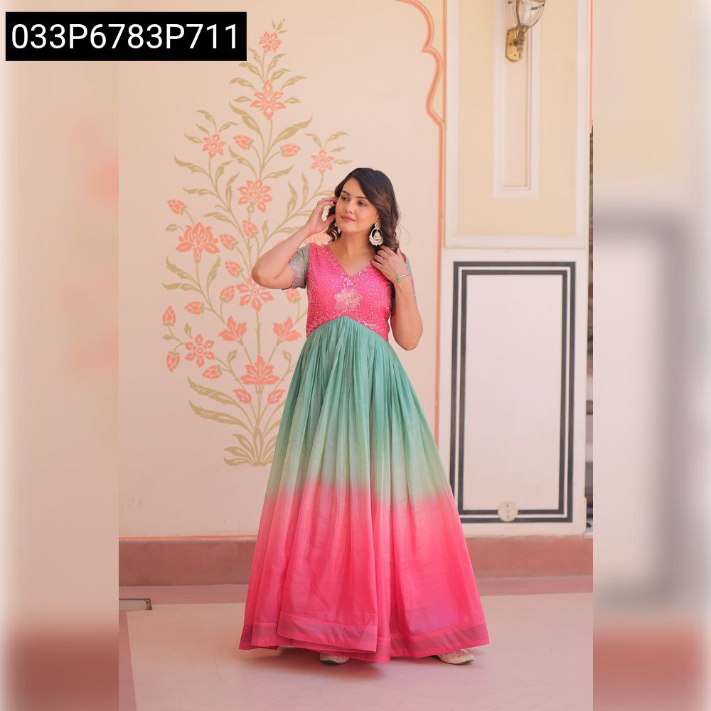 Front view of a woman in a pink and green ombré gold crush embroidered gown, posing against a patterned wall.