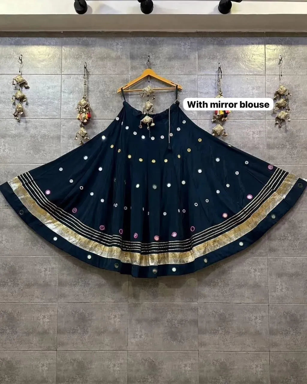 Navy blue flared cotton skirt with colorful mirror work and gold borders hanging on a rustic tiled wall
