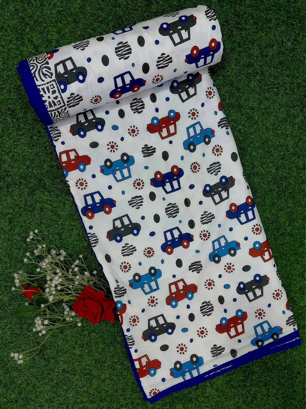 White mulmul cotton dohar folded with blue and red car print and blue border on grass