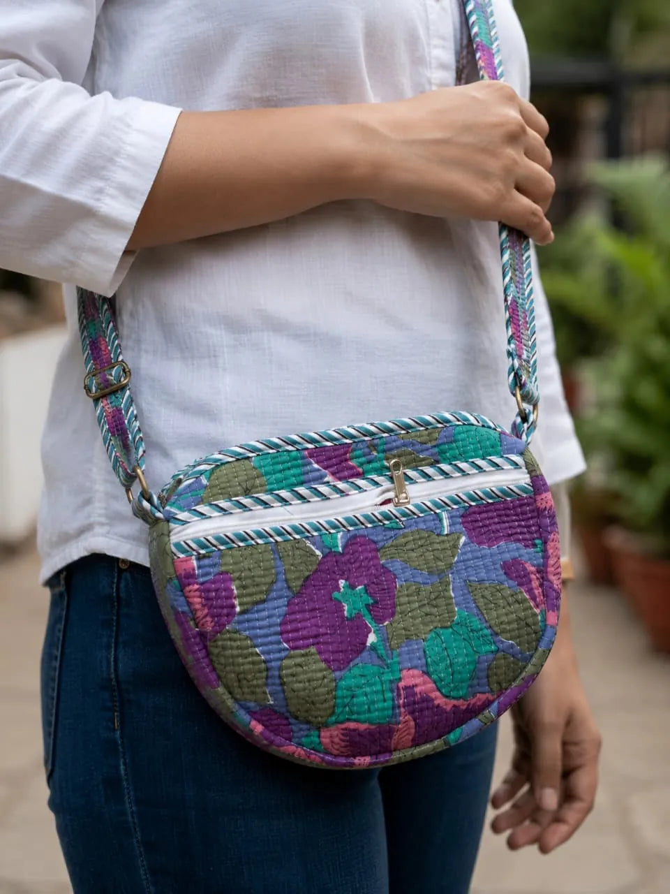 Purple and green floral hand block printed quilted banana bag worn as a crossbody sling by a model wearing a white shirt