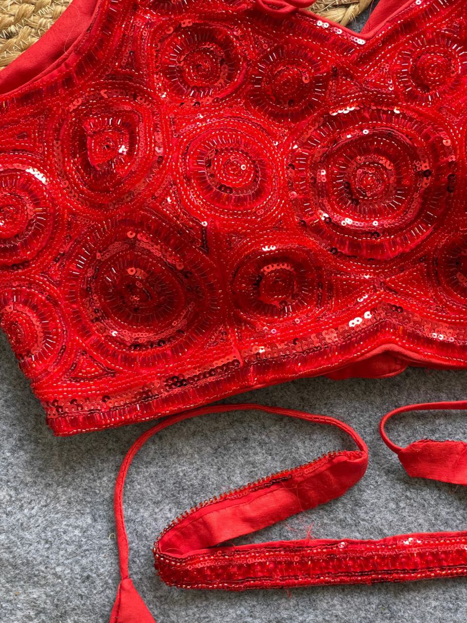 Close-up of a vibrant red heavily embellished sleeveless blouse with intricate bead and sequence work, paired with a matching waist belt.