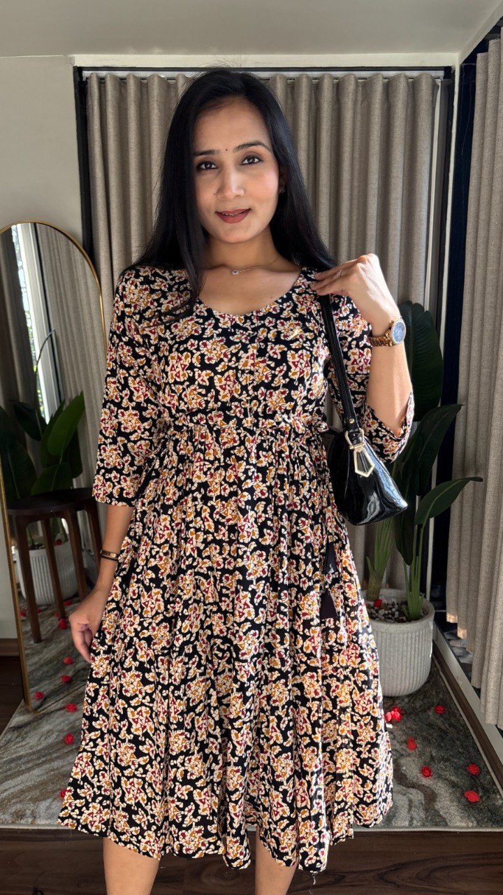 Woman posing in black multi-floral Kalamkari print pure cotton knee-length dress with adjustable belt, front view