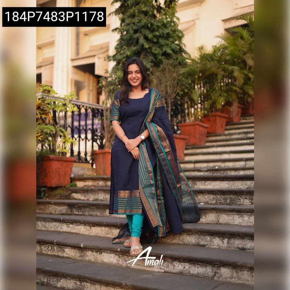 Full body shot of a smiling woman posing on steps, wearing a navy blue Kanchi Cotton suit set with a teal and gold border dupatta and matching leggings.