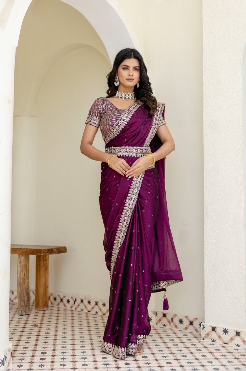 Model in deep plum purple Kasturi Silk Saree with zari, dori, and sequin work, posing gracefully in an archway.