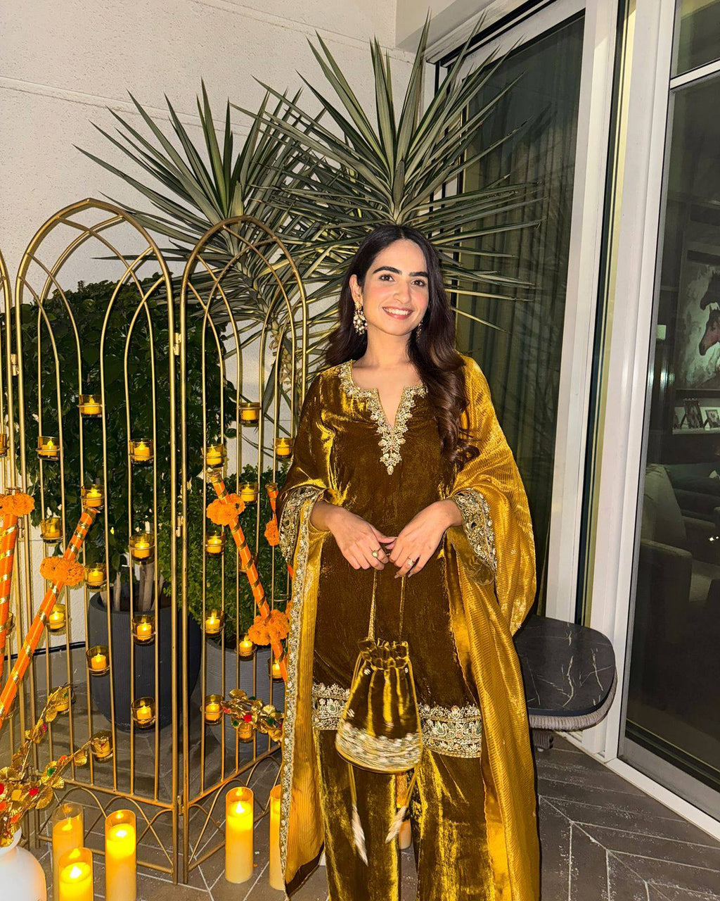 Smiling woman posing outdoors in a mustard gold velvet kurti-plazzo set with matching potli bag.