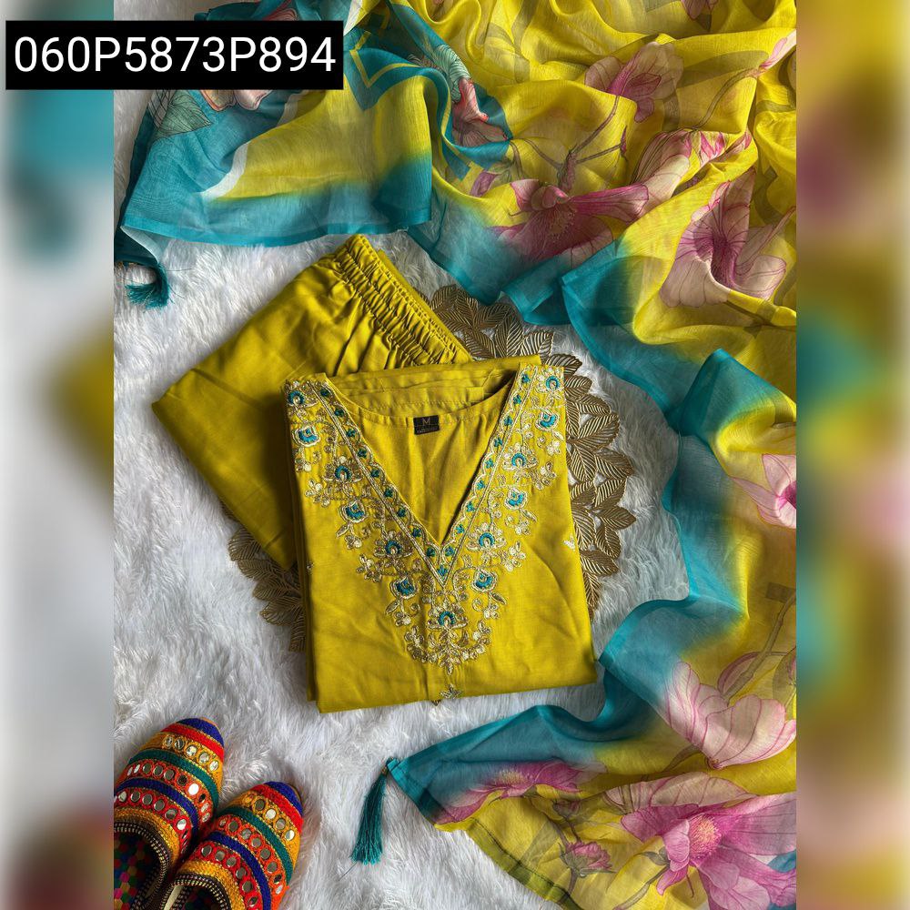 Top-down view of yellow kurti set with embroidered neckline, matching pants, floral digital print dupatta, and colorful mojari shoes on a white fluffy surface.