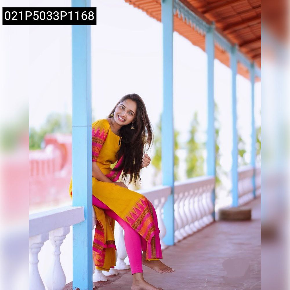 Smiling woman sitting on a railing wearing a yellow silk cotton kurti with pink jacquard weaving and pink leggings, showcasing the Laxmi kurti dupatta set.