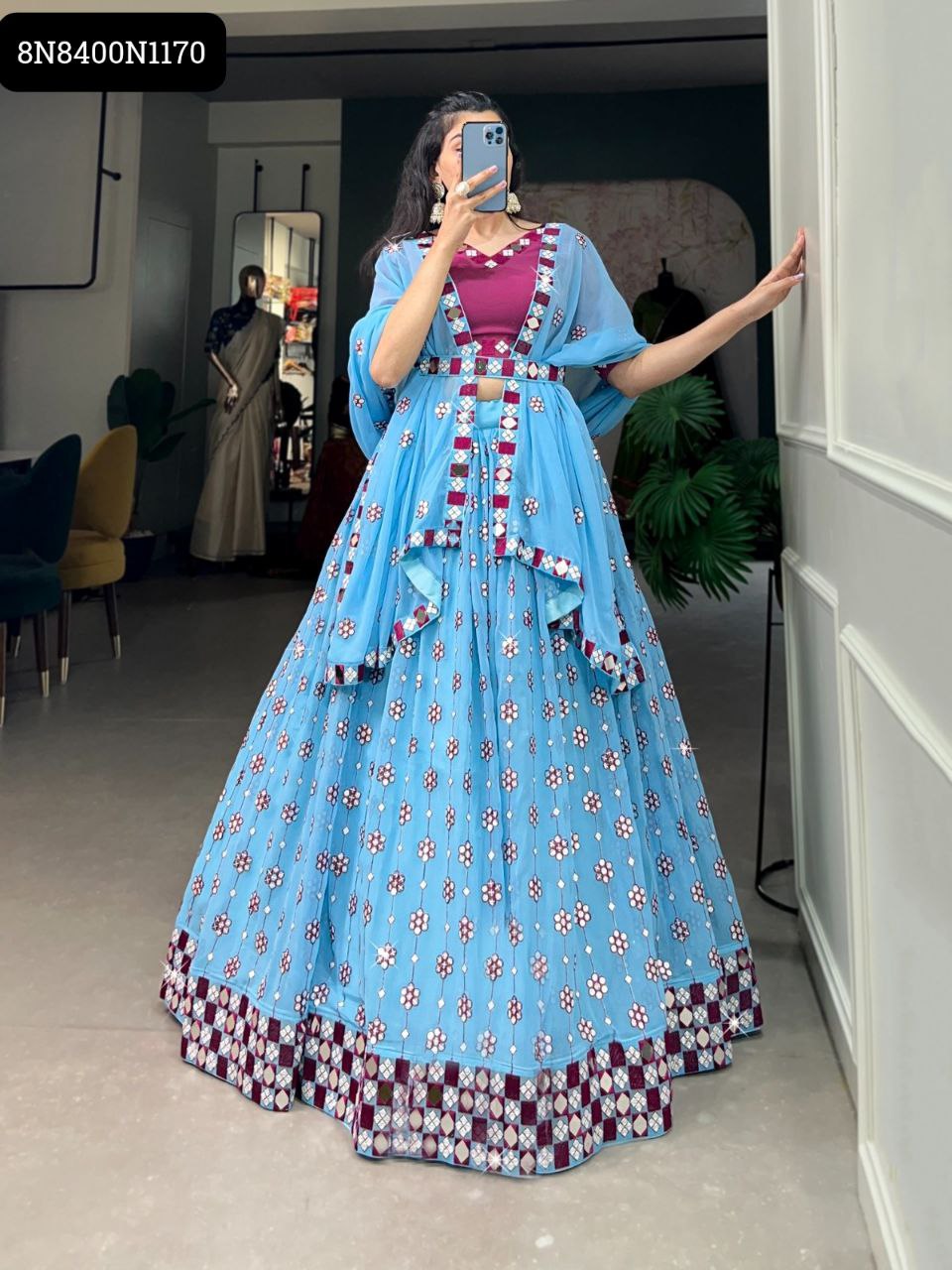 Full-length view of a woman in a sky blue sequined and embroidered georgette lehenga choli with a magenta blouse and belt, in an indoor setting.