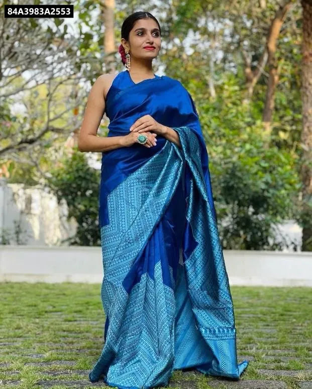 A woman wearing a vibrant blue Lichi Silk Jacquard Saree in a garden setting, looking directly at the camera.
