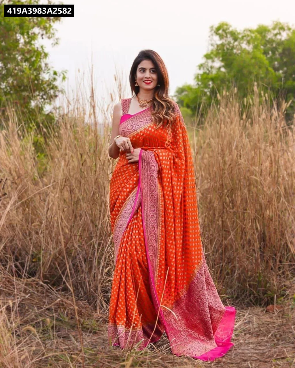 Model posing in orange Lichi silk saree with pink border, outdoor setting, TRENDBUY