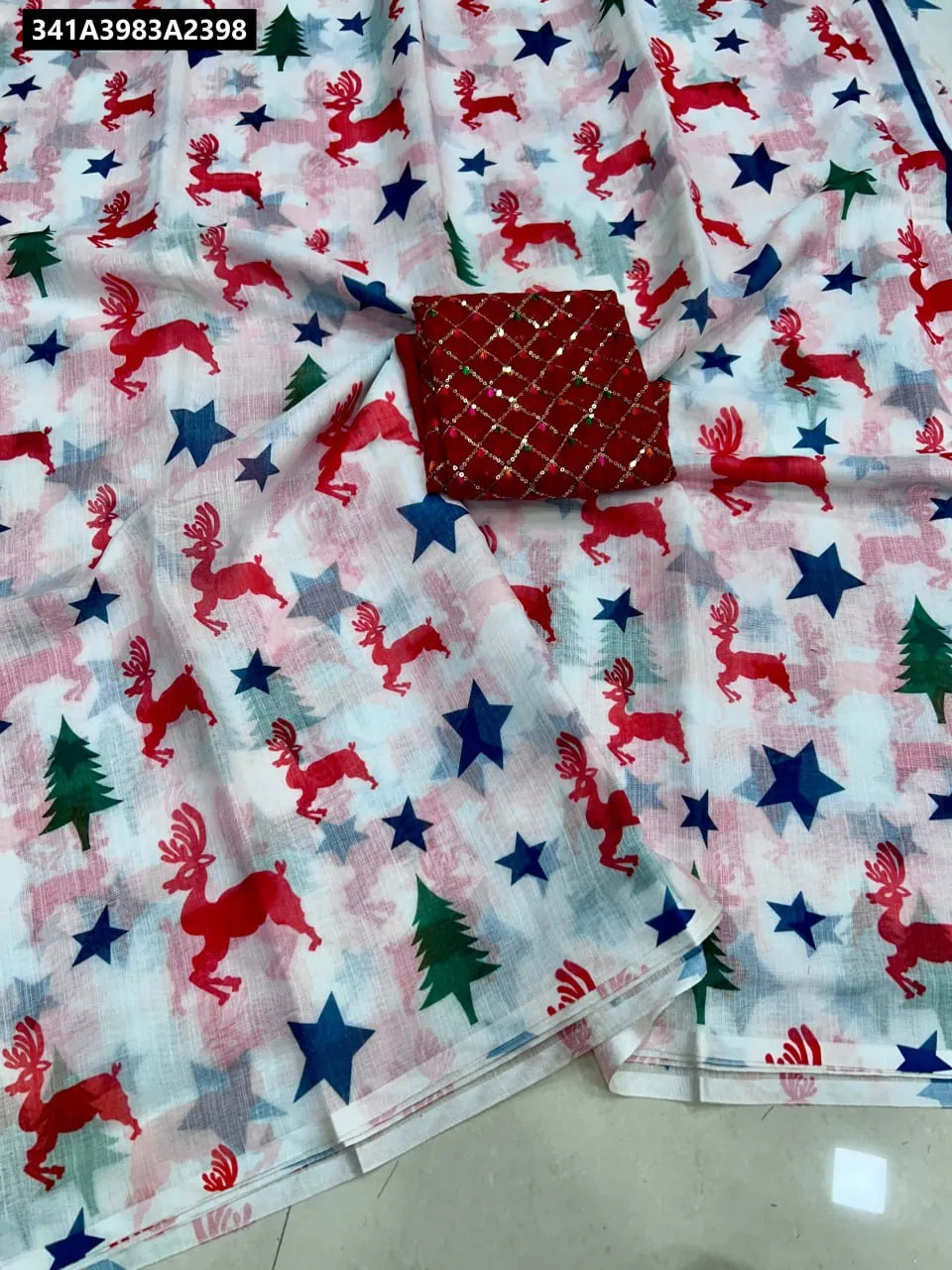 White Pure Linen Digital Print Saree with Christmas reindeer and stars, paired with a red sequin embroidered blouse. Flat lay.