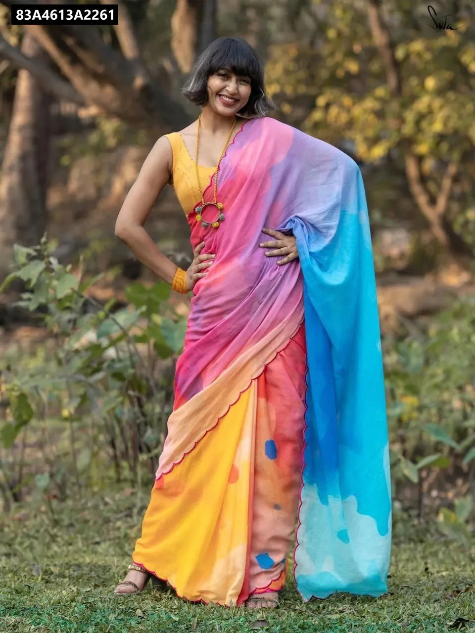 Front-facing model smiling brightly in a stunning vibrant multi-color digital print linen saree, posing in nature.