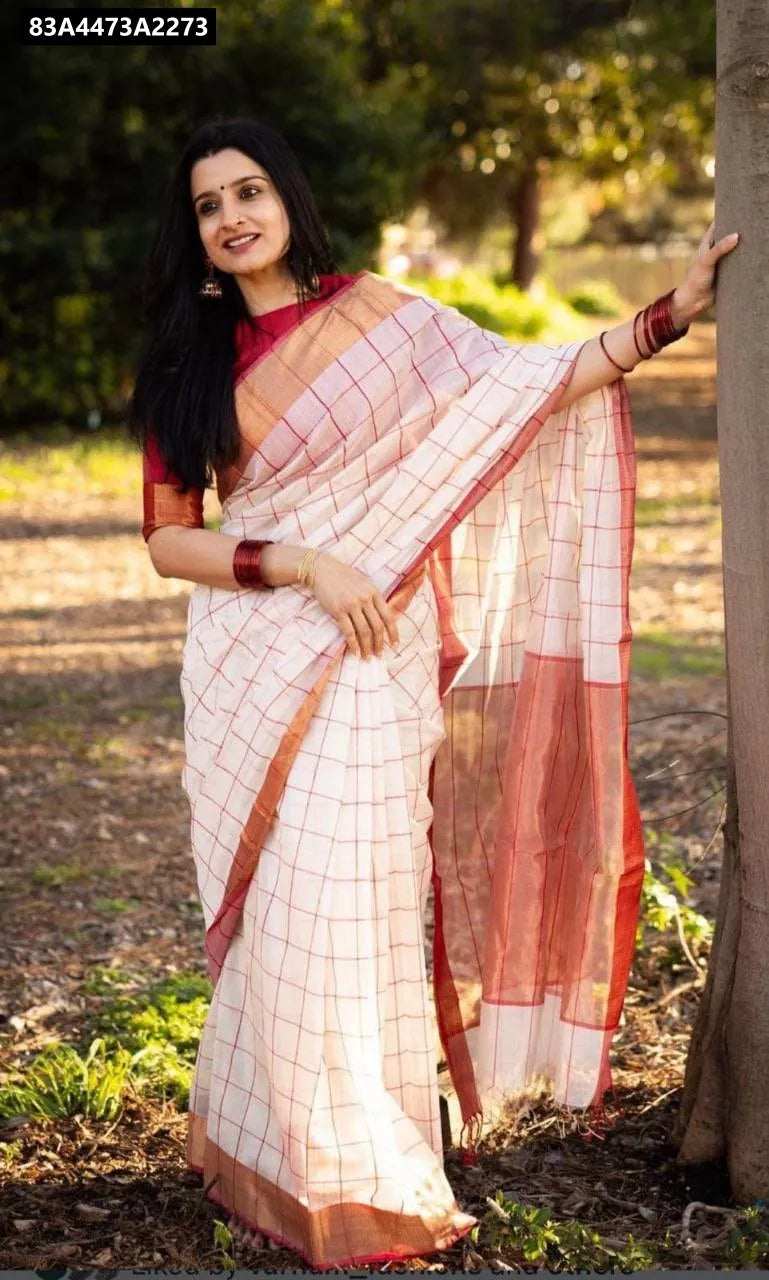 Woman wearing white and red checked linen saree with red blouse, smiling outdoors.