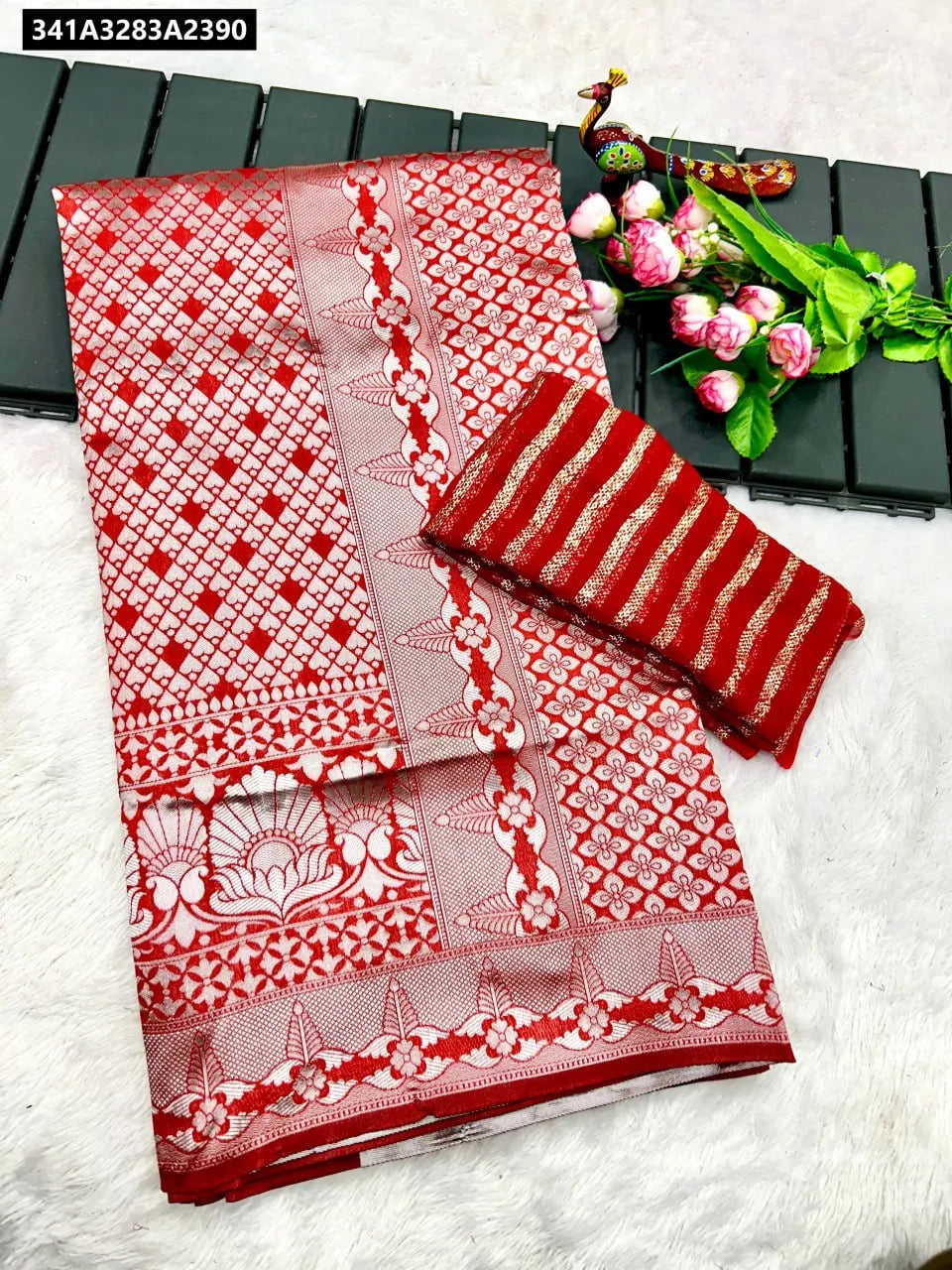 Red Litchi Silk Saree with elaborate silver woven patterns, folded with a striped red and gold blouse piece, flat lay.