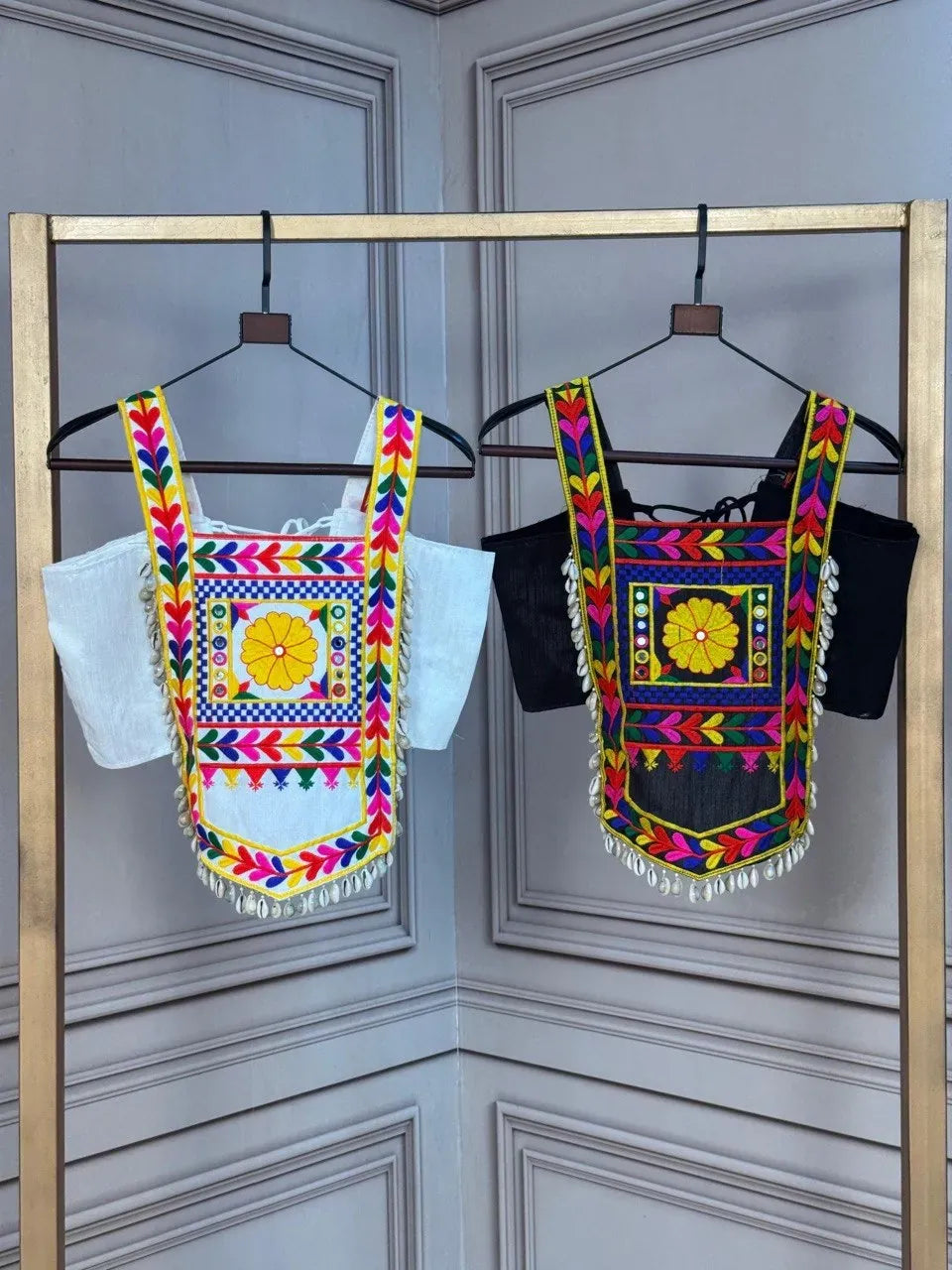 Black and white traditional embroidered crop tops with mirrors and shell fringe hanging on a display stand