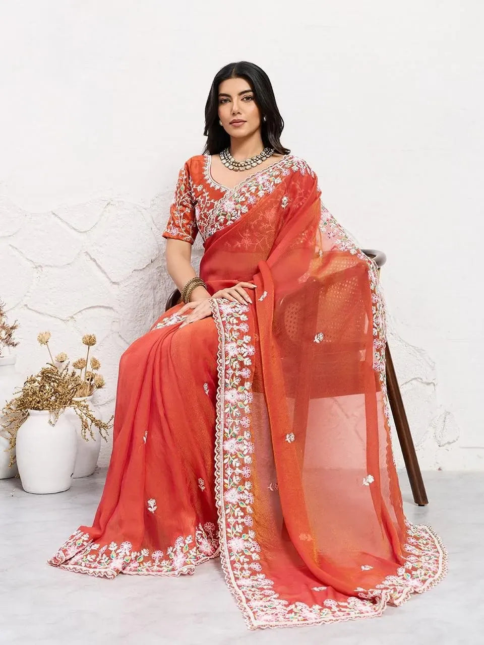 Model seated wearing rust orange embroidered chiffon saree