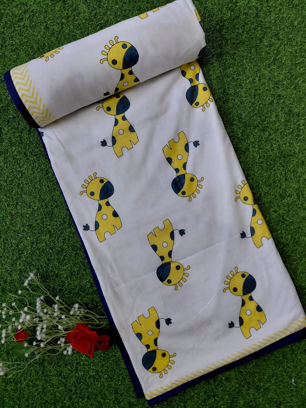 Rolled white mulmul cotton kids dohar with yellow giraffe print on grass