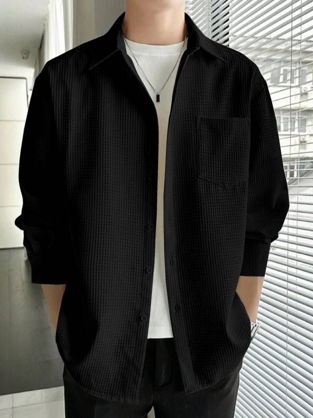 Person wearing a black textured shirt over a white shirt in an indoor setting.