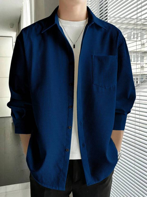 Person wearing a blue textured shirt over a white shirt in an indoor setting.