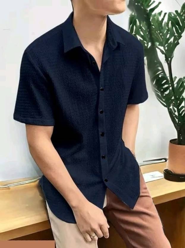 Person wearing a navy blue short-sleeve button-up shirt with a plant in the background