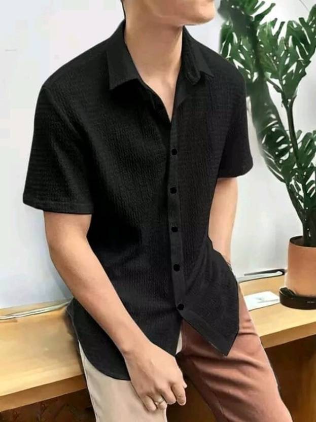 Person wearing a black short-sleeve button-up shirt with a plant in the background