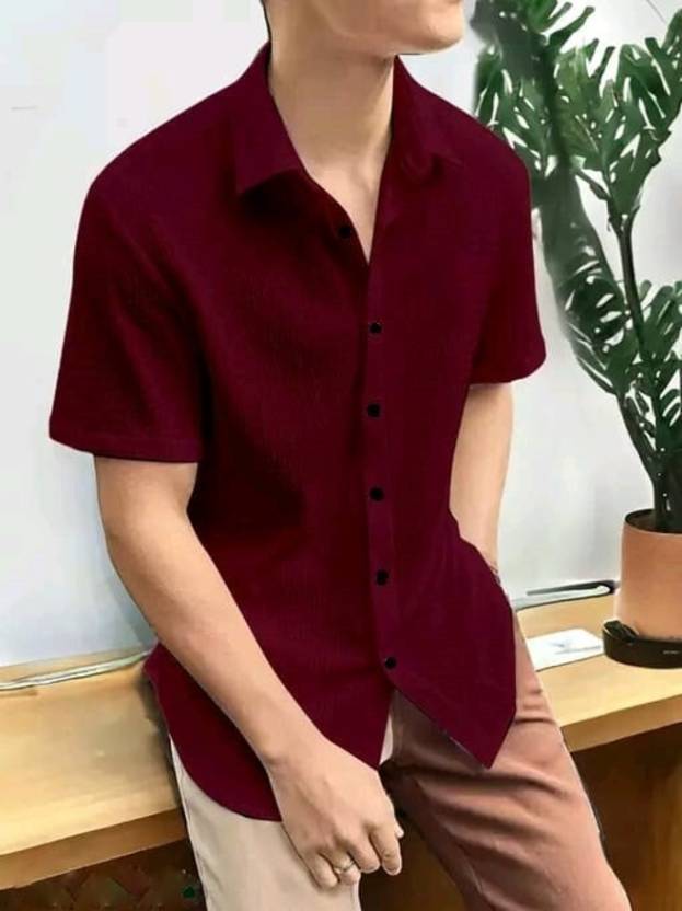 Person wearing a maroon button-up shirt with a plant in the background