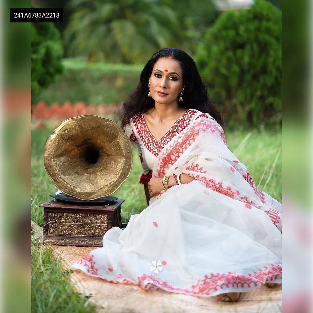 Elegant woman in a white Organza Silk Saree with red embroidery, posing with a vintage gramophone in a garden.