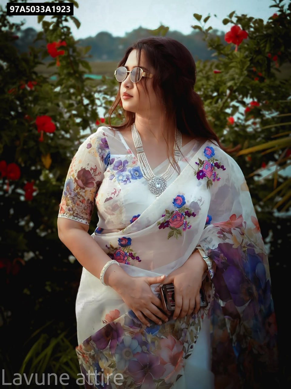Woman in white organza silk saree with colorful floral print and sunglasses, looking right