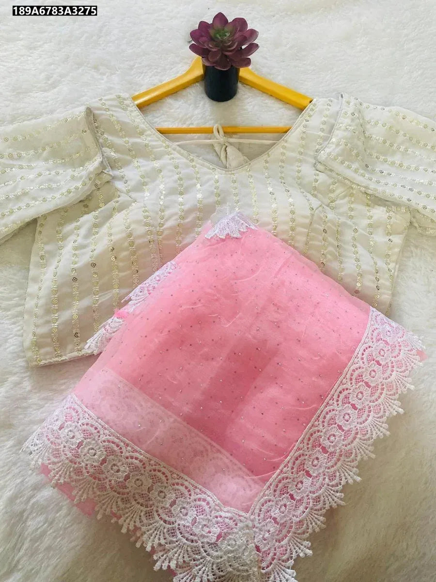 Flat lay of pink organza saree with white lace border and a white embroidered blouse on a hanger, on a white textured surface.